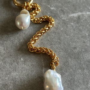 May include: A gold chain necklace with two large, irregular-shaped white pearls hanging from it. The chain is a thick, braided style.