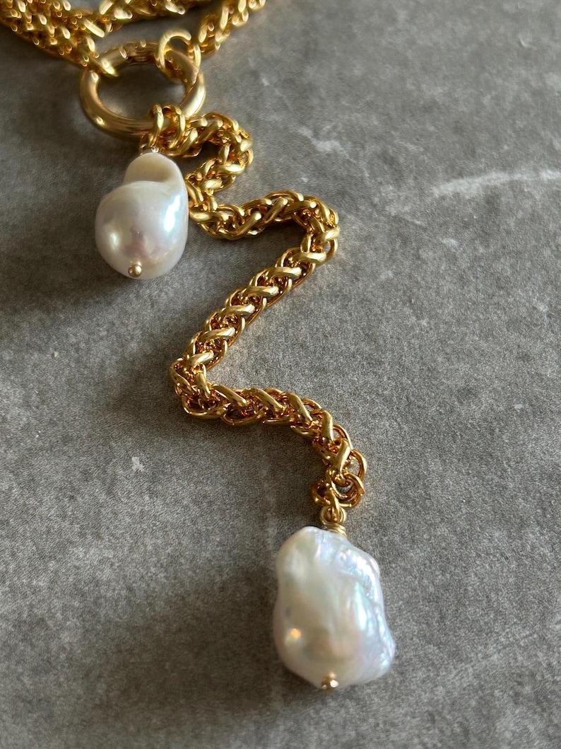 May include: A gold chain necklace with two large, irregular-shaped white pearls hanging from it. The chain is a thick, braided style.