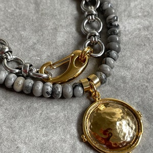 Puede incluir: Un collar de capas con una cadena de plata, cuentas de mármol gris y blanco y un colgante de oro con textura martillada.