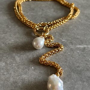 May include: A gold chain necklace with two large white baroque pearls hanging from it. The chain is double-layered and has a delicate, twisted design.