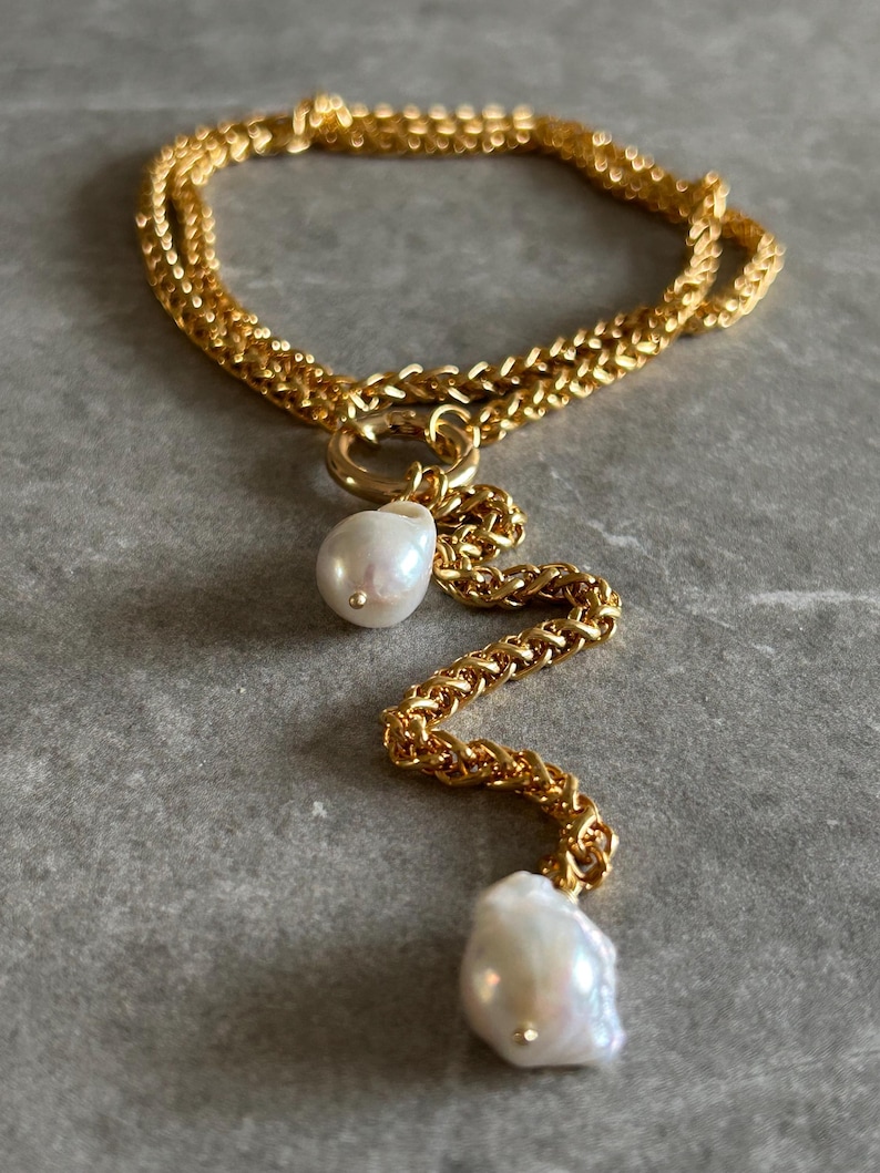 May include: A gold chain necklace with two large white baroque pearls hanging from it. The chain is double-layered and has a delicate, twisted design.