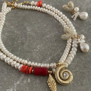 May include: A double strand pearl necklace with a variety of charms, including a coral bead, a gold fish, a gold spiral with a rhinestone, and two gold butterfly charms with rhinestones.