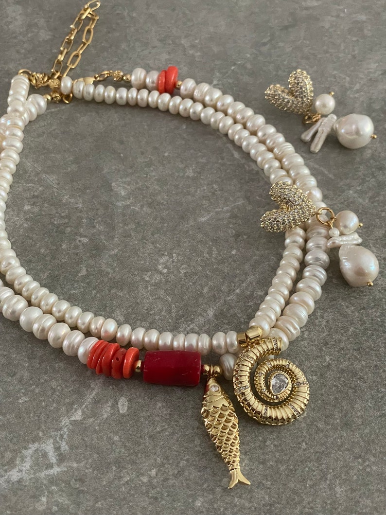 May include: A double strand pearl necklace with a variety of charms, including a coral bead, a gold fish, a gold spiral with a rhinestone, and two gold butterfly charms with rhinestones.