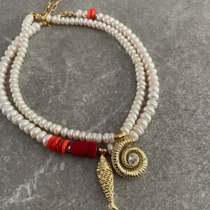 May include: A double strand pearl necklace with a red coral bead and gold charms, including a fish and a spiral shell with a clear rhinestone.