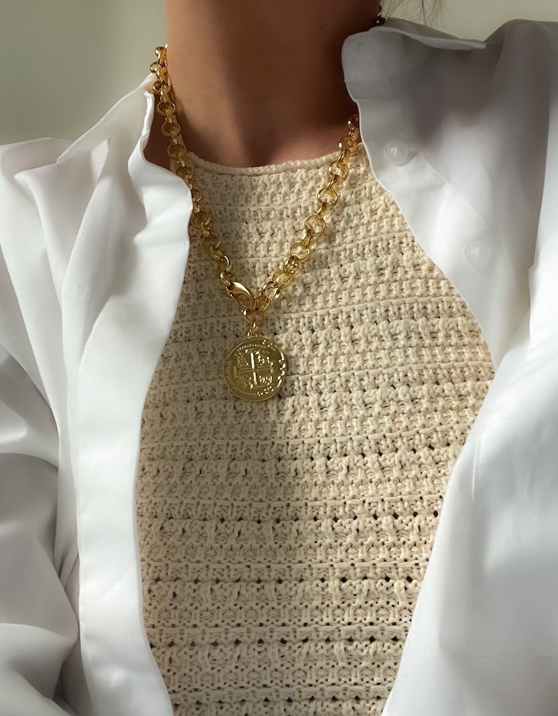 May include: A gold chain necklace with a large gold coin pendant. The chain is thick and has a chunky link design. The coin pendant has a detailed design and is hanging from the chain with a clasp.