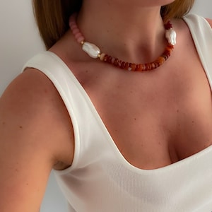 May include: A multi-coloured beaded necklace with two large white pearl accents. The necklace is made of pink, orange and brown beads.
