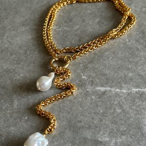 May include: A gold chain necklace with two large white pearls hanging from it. The chain is a double chain with a twisted design. The pearls are irregular in shape and have a natural, organic look.