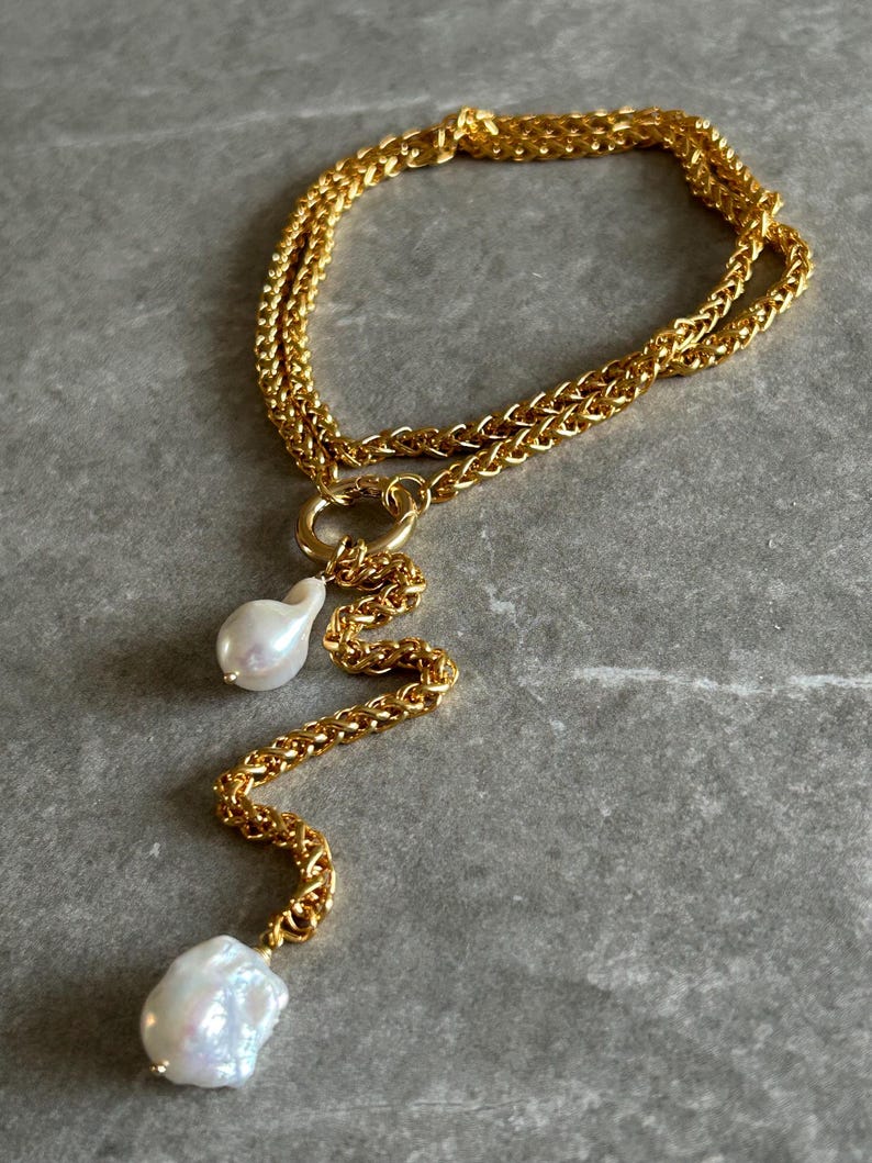 May include: A gold chain necklace with two large white pearls hanging from it. The chain is a double chain with a twisted design. The pearls are irregular in shape and have a natural, organic look.