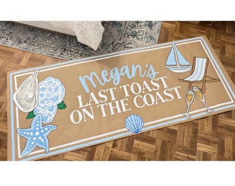May include: A rectangular, beach-themed rug with the text "Megan's LAST TOAST ON THE COAST" in light blue. The rug features illustrations of a sailboat, beach chair, champagne flutes, starfish, and seashells.