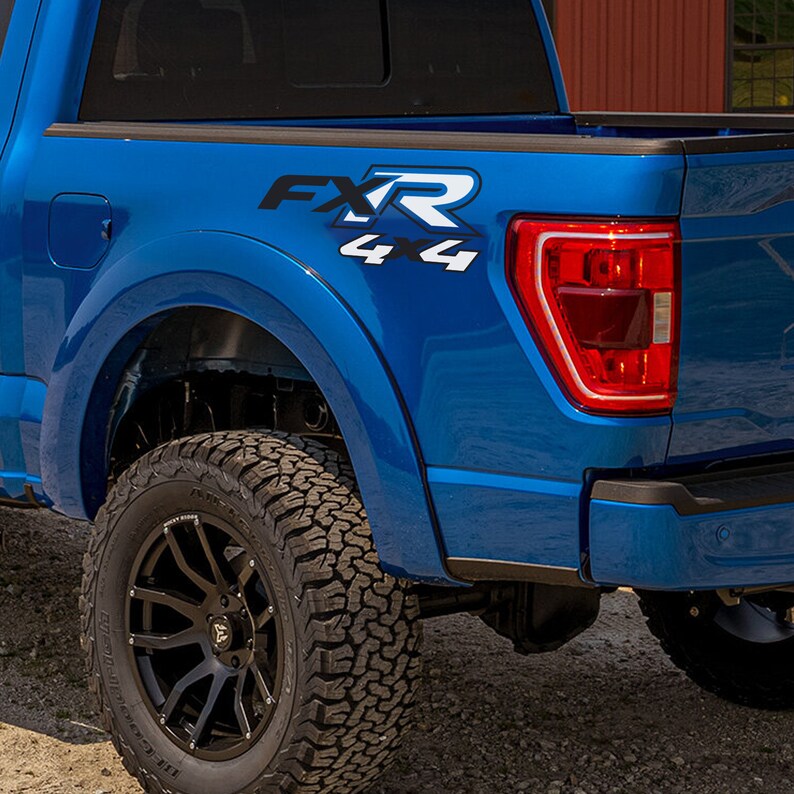 May include: A close-up of the rear quarter panel of a bright blue pickup truck. The truck has black wheels with large, off-road tyres. The text "FXR 4x4" is displayed in black and white on the side of the truck.