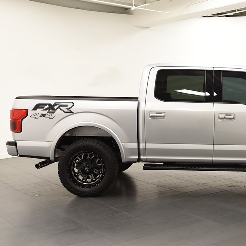 May include: Silver pickup truck with black wheels and tyres. The truck has the text "FXR 4x4" in black on the side. The truck has a black step bar and tinted windows.