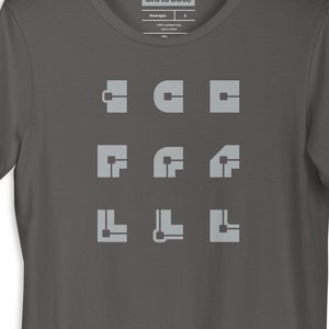 Può includere: Una t-shirt grigio antracite con un design grafico di nove forme geometriche di colore grigio chiaro. Le forme sono disposte in tre file di tre. Il testo "chris cote" è stampato sull'etichetta.