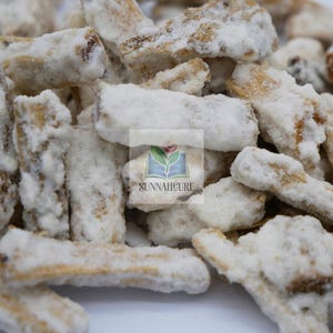 Puede incluir: Primer plano de trozos de fruta seca azucarada. Los trozos son de color marrón claro y están cubiertos con una gruesa capa de azúcar blanca. La imagen incluye el texto "SUNNAHCURE" con un logotipo de un libro y una rosa.