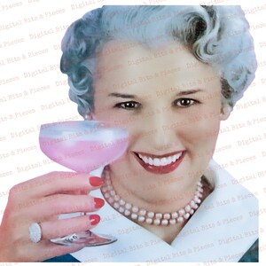 May include: A woman with white hair and a pearl necklace smiles while holding a pink cocktail in a clear glass. She is wearing red nail polish and a ring on her finger.
