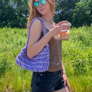 Puede incluir: Una mujer con un top de tirantes de estampado de leopardo, pantalones cortos de mezclilla y gafas de sol sostiene una bolsa de mano de crochet morado y una taza de caf&eacute; helado.