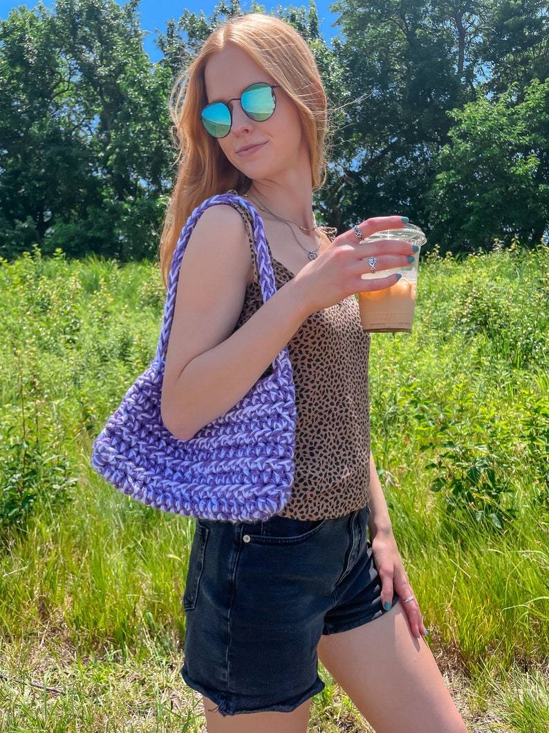 Puede incluir: Una mujer con un top de tirantes de estampado de leopardo, pantalones cortos de mezclilla y gafas de sol sostiene una bolsa de mano de crochet morado y una taza de caf&eacute; helado.