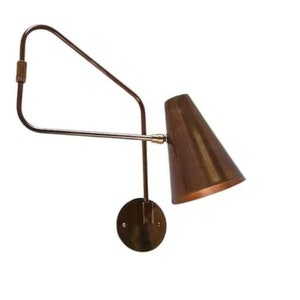 Puede incluir: Una lámpara de pared de latón con una pantalla en forma de cono. La lámpara tiene un brazo largo y ajustable que se puede colocar para dirigir la luz.