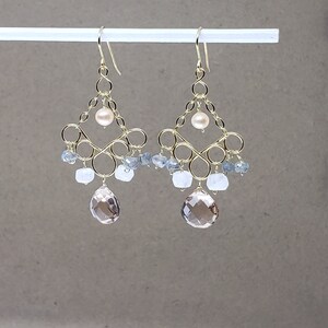 May include: Gold dangle earrings with a geometric design featuring a pearl and multiple light blue and brown gemstones.