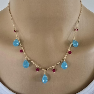 May include: A gold chain necklace with blue teardrop-shaped stones and small red beads.