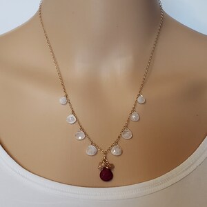 Op de afbeelding: Een gouden ketting met een rode edelsteen hanger en witte traanvormige stenen.