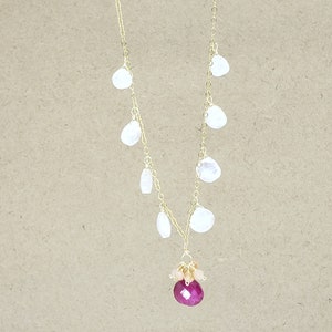 Op de afbeelding: Een gouden ketting met een cluster van kleine witte stenen en een grote roze edelsteen hanger.