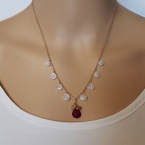 May include: A gold chain necklace with a red gemstone pendant and white gemstone accents.