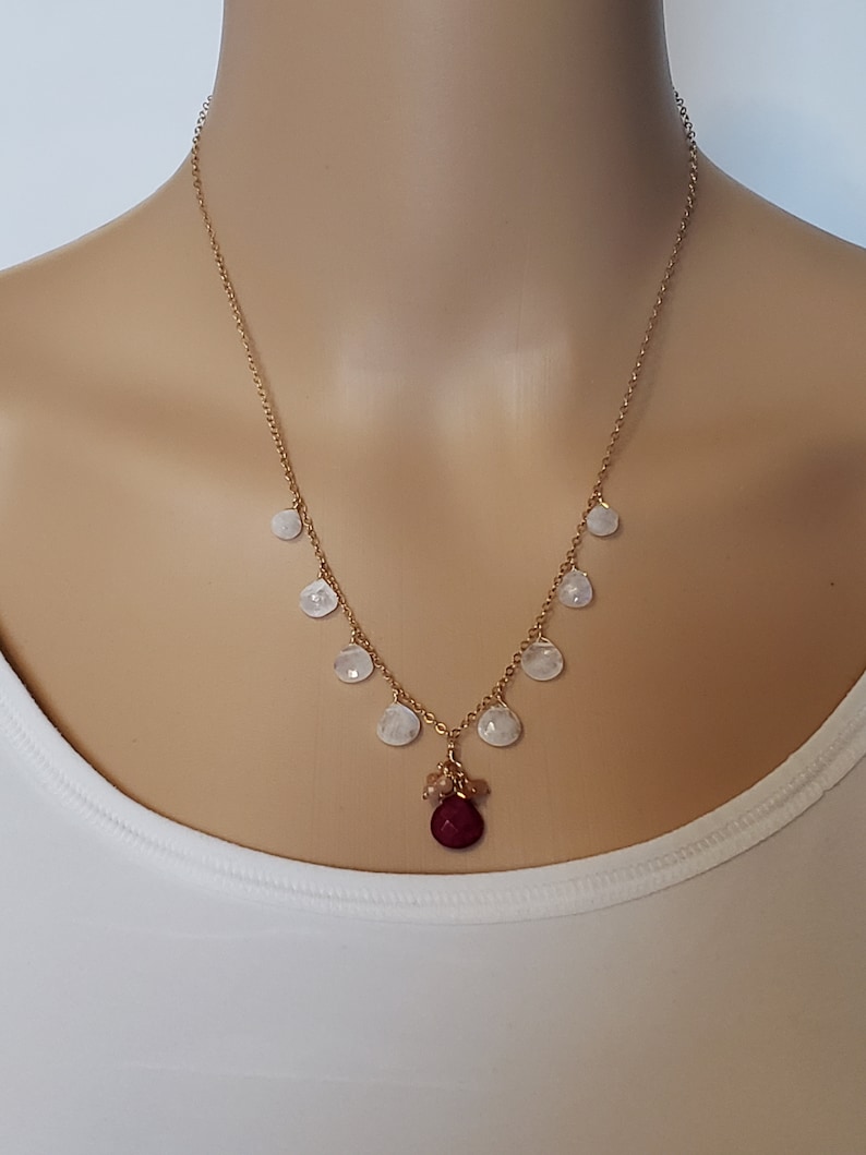 Op de afbeelding: Een gouden ketting met een rode edelsteen hanger en witte edelsteen accenten.