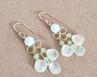 May include: Gold dangle earrings with light blue and green gemstone beads. The earrings feature a delicate, twisted wire design.