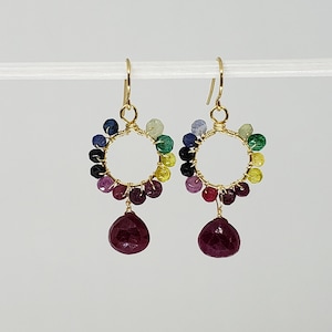 May include: A pair of gold-coloured hoop earrings. Each earring has a halo of colourful beads and a large, faceted, teardrop-shaped, deep red gemstone pendant. The earrings are suspended from gold-coloured ear wires.