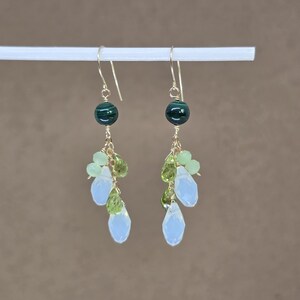 May include: A pair of gold-toned dangle earrings. Each earring features a dark green bead at the top, followed by clusters of light green and pale blue teardrop-shaped beads. The earrings are suspended from gold-colored ear wires.