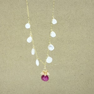 Op de afbeelding: Een gouden ketting met een roze edelsteen hanger en witte edelsteen accenten. De ketting heeft een cluster van kleinere roze edelstenen die de grotere roze edelsteen omringen.