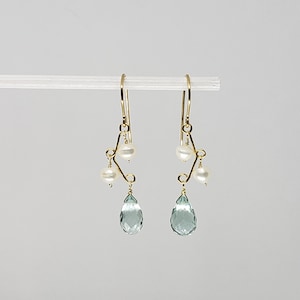May include: Gold earrings with a teardrop shaped aquamarine gemstone and three white pearls hanging from a delicate wire design.