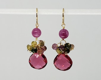 May include: Gold earrings with pink and green gemstones. The earrings feature a large pink teardrop-shaped gemstone and a smaller pink round gemstone. The earrings are accented with smaller green and pink gemstones.