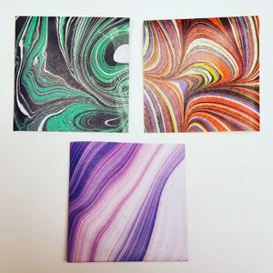Peut inclure: Trois carrés de papier décoratifs avec des motifs marbrés. Le premier carré est vert et noir, le deuxième est orange, jaune et violet, et le troisième est violet et blanc.