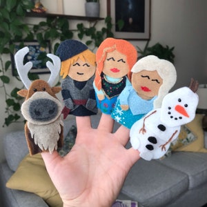 Könnte beinhalten: Ein Set aus fünf Filz-Fingerpuppen mit Figuren aus einem beliebten Animationsfilm. Die Puppen zeigen ein Rentier, eine Figur mit blonden Haaren, eine Figur mit roten Haaren, eine Figur mit weißen Haaren und einen Schneemann, alle mit lächelnden Gesichtern.