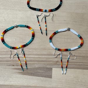 May include: Three beaded necklaces with matching earrings. The necklaces are made with colorful beads in a rainbow pattern. The earrings are long and dangle.