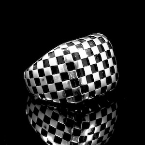 May include: A silver ring with a checkered pattern in black and white.