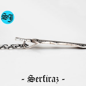 May include: Silver pendant necklace with a detailed, ornate design. The pendant is shaped like a sword and has a chain attached.