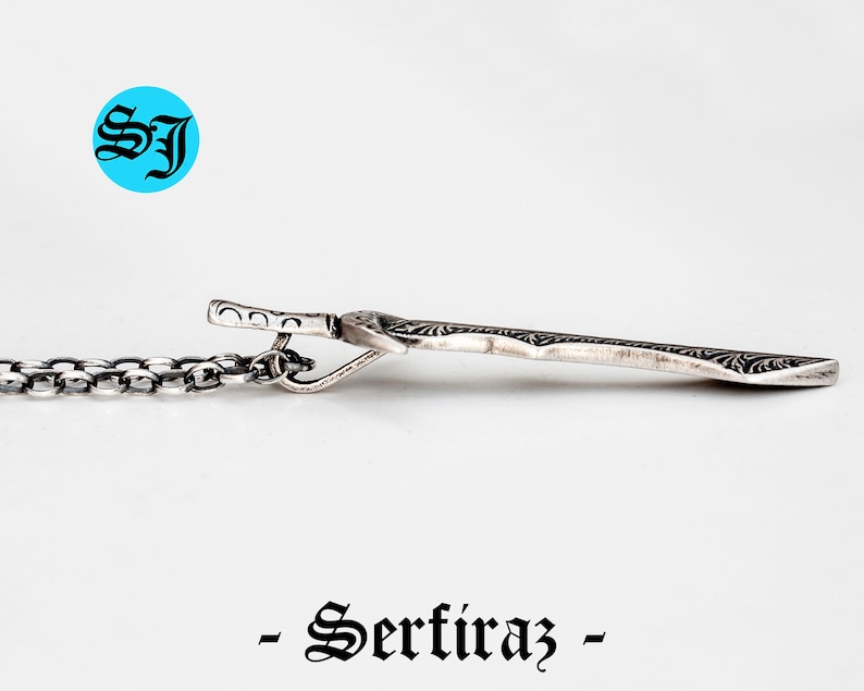 May include: Silver pendant necklace with a detailed, ornate design. The pendant is shaped like a sword and has a chain attached.