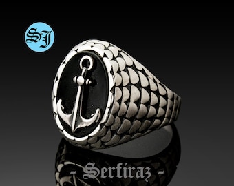 Puede incluir: Un anillo de plata con una piedra de ónix negro con un diseño de ancla de plata. La banda del anillo tiene un patrón texturizado.