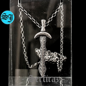May include: A silver sword pendant necklace with an intricate design. The pendant is hanging from a silver chain.