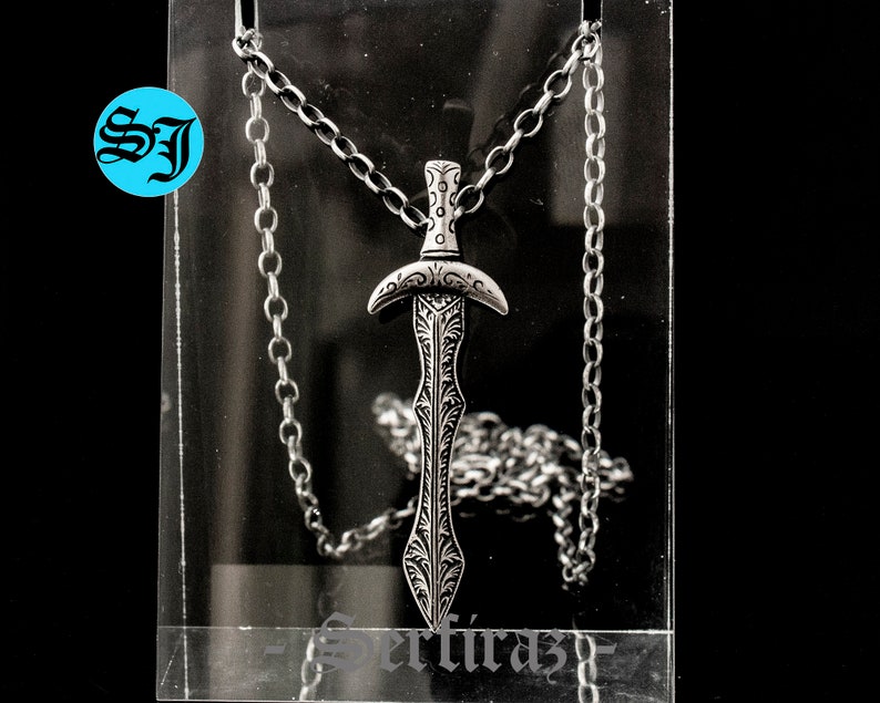 May include: A silver sword pendant necklace with an intricate design. The pendant is hanging from a silver chain.