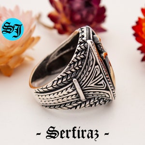 May include: A silver ring with intricate engraved patterns and a gold-colored triangular centerpiece. The ring features a detailed design on the band and a contrasting gold accent. The word "- Serfiraz -" is printed at the bottom.