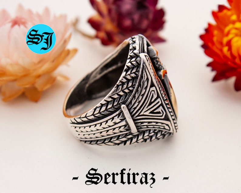 May include: A silver ring with intricate engraved patterns and a gold-colored triangular centerpiece. The ring features a detailed design on the band and a contrasting gold accent. The word "- Serfiraz -" is printed at the bottom.