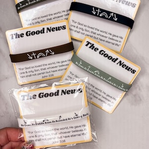 以下が含まれることがあります： 「The Good News」のテキストと聖書の詩が書かれたカードで、それぞれにマッチするゴムバンドが付いています。バンドは黒、茶色、緑など様々な色があり、宗教的なシンボルとテキストが描かれています。