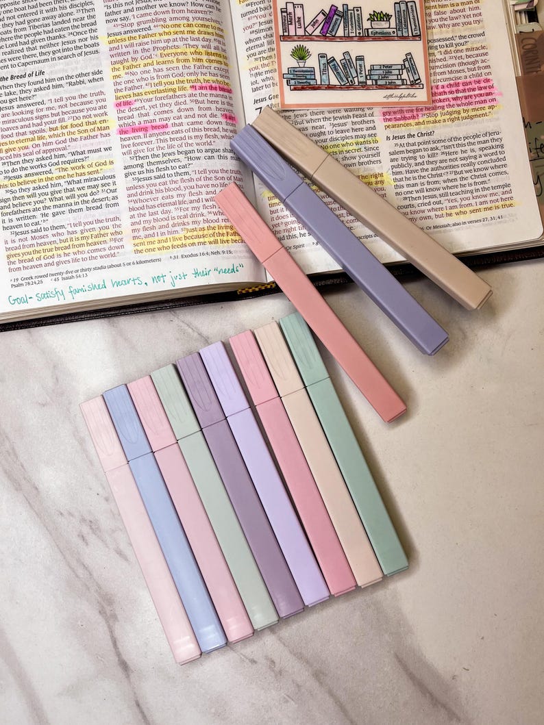 May include: An open book with highlighted text and colorful highlighters. The highlighters are in shades of pink, purple, beige, and green. The text on the page is partially visible.