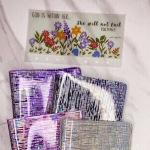 May include: Four clear plastic binders with iridescent holographic stripes. The binders are stacked on top of each other. The top binder has a clear plastic insert with a floral design and the text "GOD IS WITHIN HER... she will not fail PSALM 146:5"