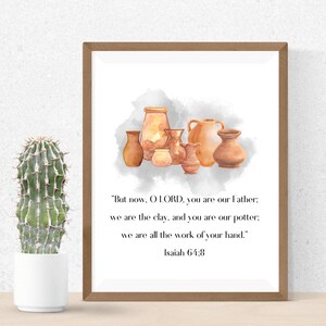 May include: A framed print featuring a watercolor illustration of various brown pottery vessels. The artwork includes the text "But now, O LORD, you are our Father; we are the clay, and you are our potter; we are all the work of your hand." Isaiah 64:8.