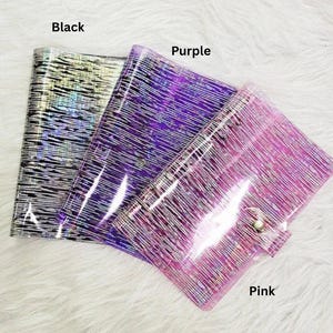 May include: Three clear, glittery pouches in black, purple, and pink. Each pouch has a textured, linear pattern and a snap closure. The colors are labeled on the image.