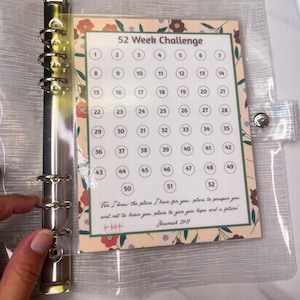 May include: A clear plastic binder with a metal six-ring mechanism containing a 52 Week Challenge tracker sheet. The sheet features a floral border, numbered circles from 1 to 52, and the text: For I know the plans I have for you.